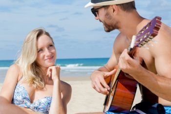 happy of man and woman playing guitar on the beach