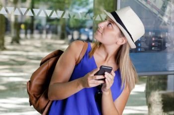 attractive young woman using smartphone while waiting in bus stop