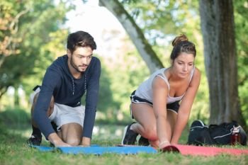 smiling woman with personal trainer doing exercises on mat outdoors