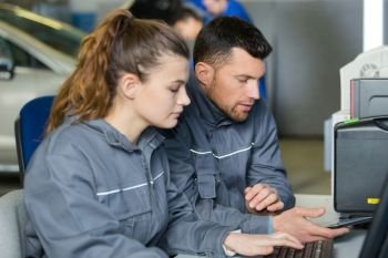 mechanic and apprentice sat at computer desk looking at smartphone