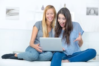 two happy young friends with laptop at home