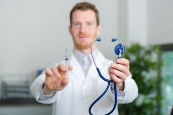confident young male doctor with stethoscope holding syringe