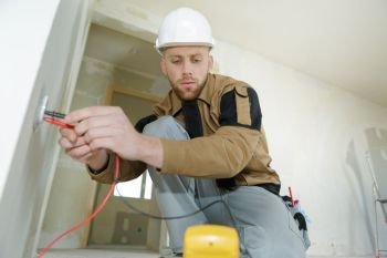 electrician checking socket voltage using multimeter in a wall fixture