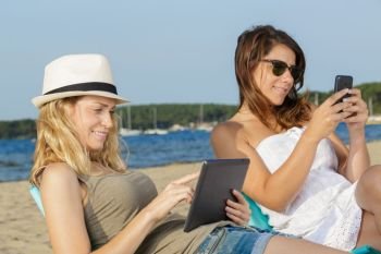 two women reading book and e-book on sea shore