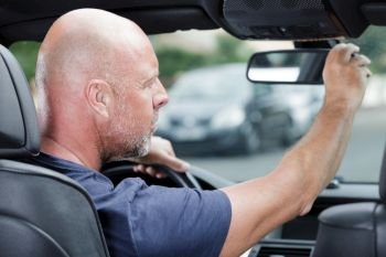 mature man adjusting the rear view mirror in car