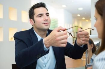 optician fitting eyeglasses on female customer