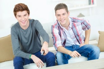 young men holding remote control and watching tv