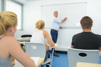 Teacher writing on white board in front of class