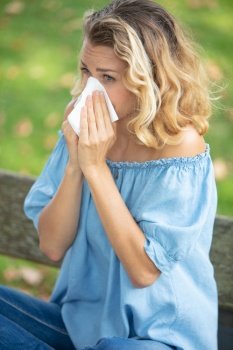 young woman sneezing outdoor while having an allergy