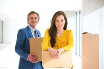 Portrait of confident businesswoman and male colleague with cardboard boxes in new office