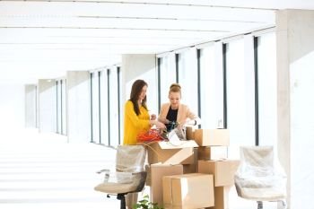 Young businesswomen untangling cords while standing by cardboard boxes in office