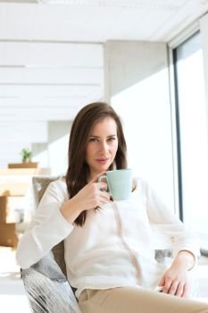 Portrait of beautiful young businesswoman drinking coffee in new office