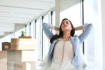 Relaxed young businesswoman with hands behind head in new office