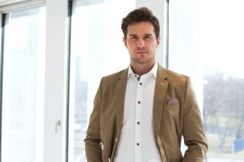Portrait of confident young businessman standing against office window