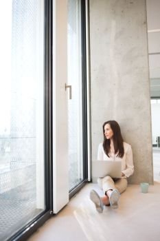 Full length of young businesswoman with laptop looking through window in new office