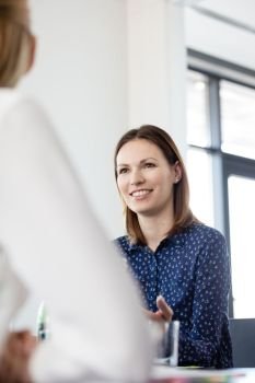 Confident young businesswoman talking with female colleague in meeting room