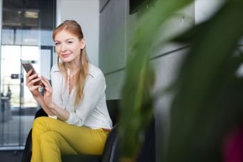Portrait of smiling young businesswoman using mobile phone on chair in office