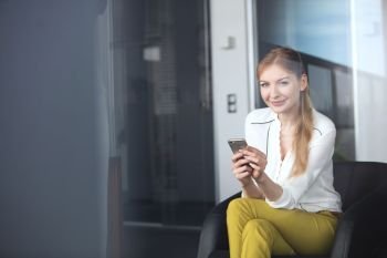 Portrait of confident young businesswoman using mobile phone on chair in office