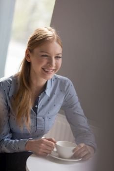 Smiling young businesswoman having coffee at table in office