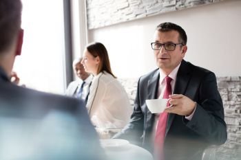 Mature businessman having coffee while talking with male colleague in office cafeteria