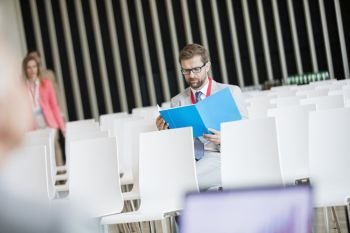Businessman reading file while sitting in seminar hall at convention center