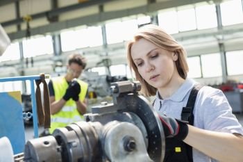 Mature female worker working on machinery with colleague in background at industry