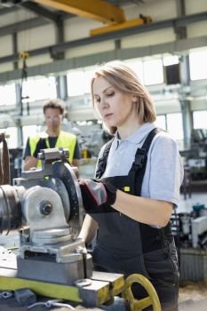 Mature female worker working on machinery with colleague in background at factory
