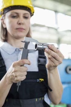 Mature female worker measuring metal with caliper in factory