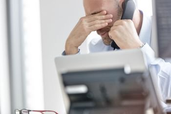 Exhausted businessman using landline phone in office