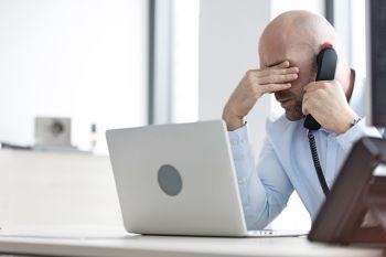 Tired mid adult businessman using telephone at desk in office