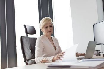 Mature businesswoman reading document at desk in office