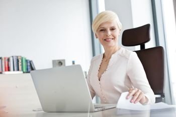 Portrait of smiling mature businesswoman with laptop and document at office desk