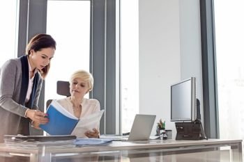 Businesswoman and female manager reading book at desk in office