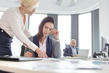 Businesswomen discussing over project with male colleague in background at office