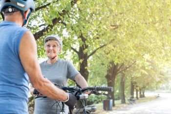 Smiling senior woman looking at man with bicycle in park