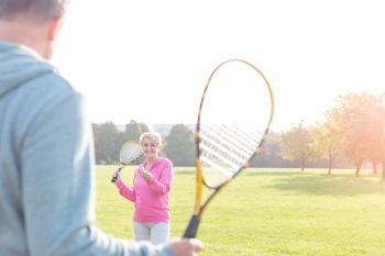 Smiling senior woman serving badminton in park