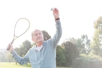 Confident senior man serving badminton in park