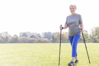 Active senior woman with trekking poles walking in park