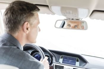 Businessman looking into rear-view mirror of car