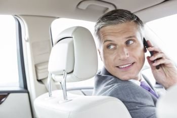 Smiling mature businessman talking on smartphone while sitting in car