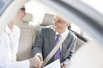 Smiling business partners shaking hands while sitting in car