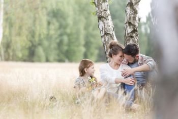 Daughter looking at loving parents while sitting on field at farmland