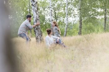 Woman sitting while man playing with daughter on field amidst trees at farmland