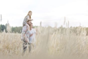 Father carrying daughter on shoulders with woman at wheat farm