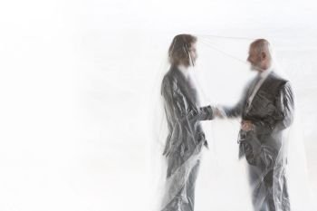 Business people under the foil. Warsaw, Poland.. Male business colleagues shaking hands while covered in plastic at office