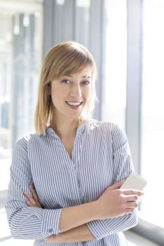 Portrait of smiling businesswoman holding mobile phone while standing at office