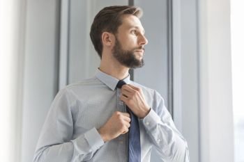 Thoughtful businessman looking away while adjusting tie at office