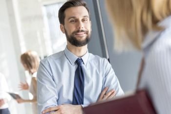 Smiling businessman listening to colleague in office corridor