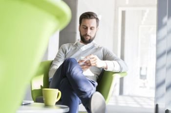 Confident businessman using smart phone in coffee break at office