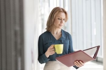 Businesswoman reading file having coffee at office